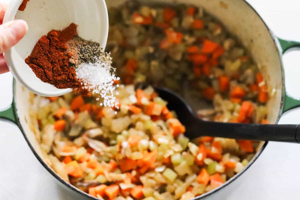 hand sprinkling a bowl of spices into a pot of chicken hash.