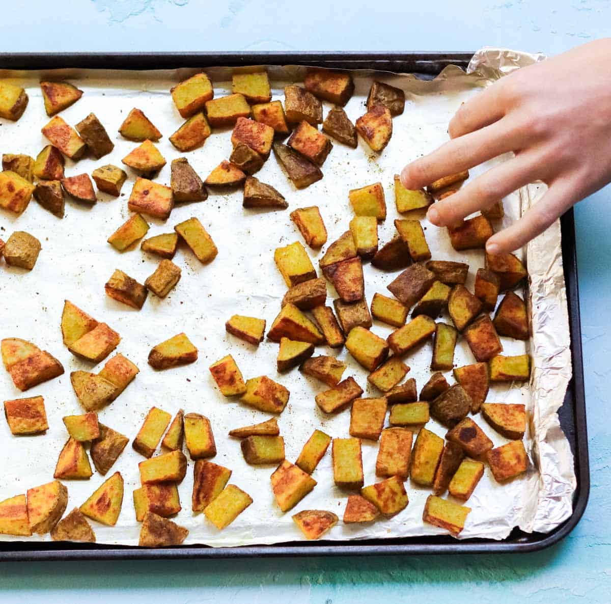hand grabbing a curry roast potato off the baking sheet.