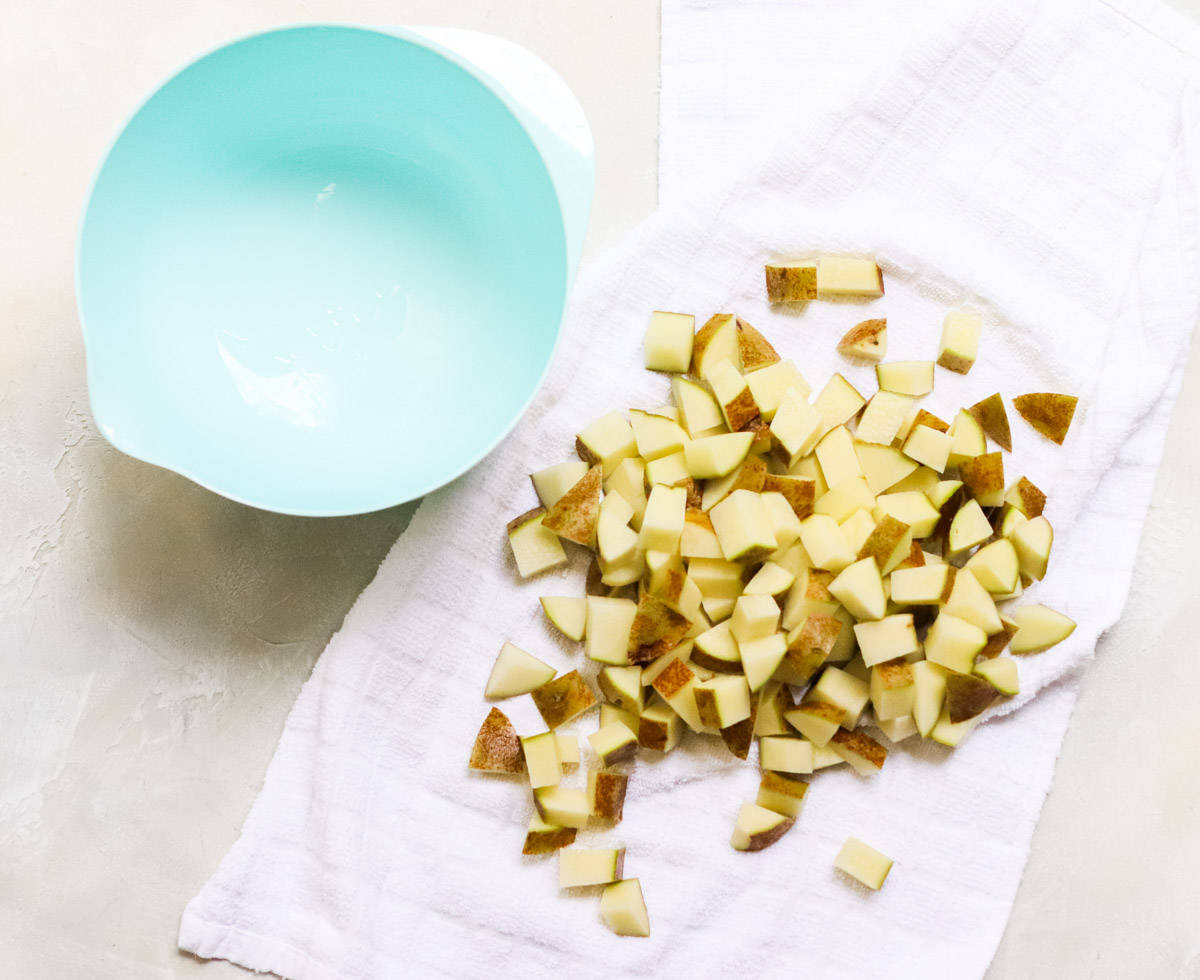 chopped potatoes drying on a dish towel next to an empty blue mixing bowl.