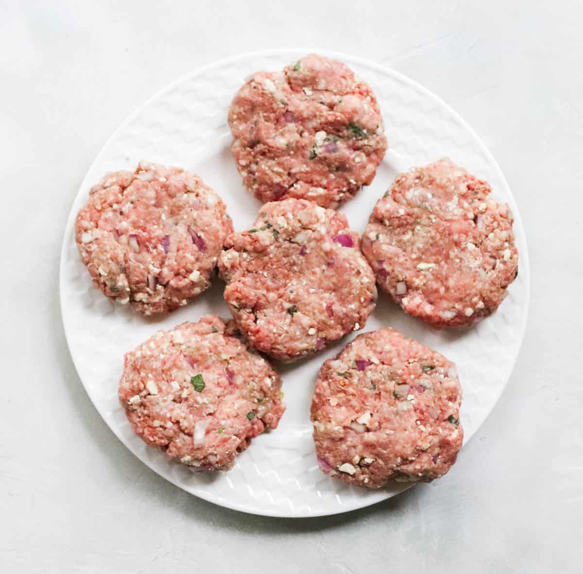 white plate with six lamb burgers before cooking.