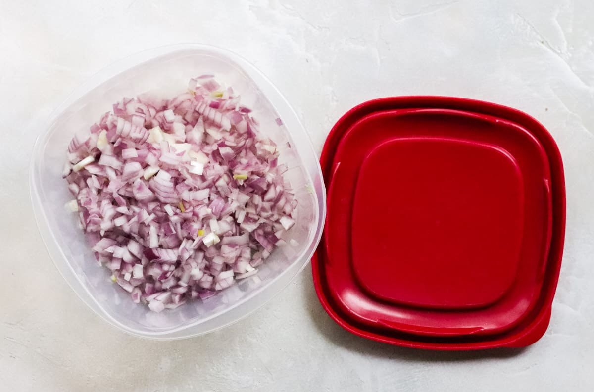 plastic container filled with diced red onion next to a red container top on a white counter.
