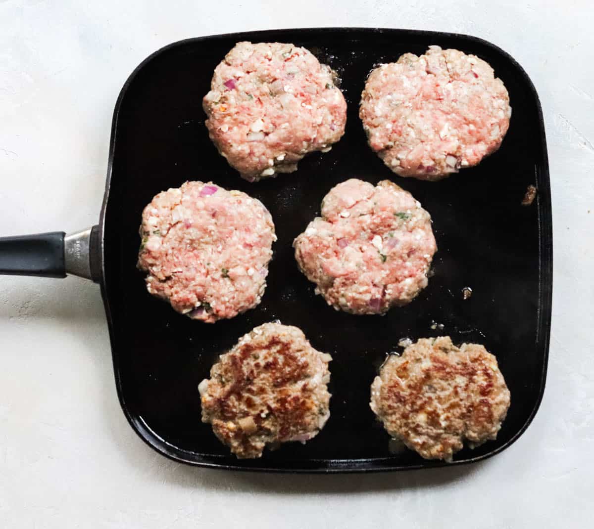 six lamb burgers cooking on a skillet.
