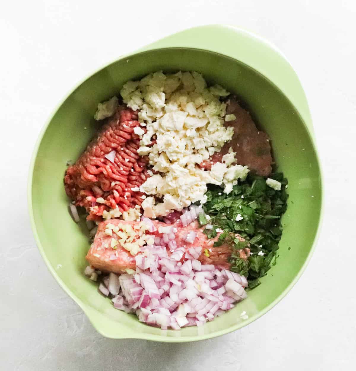 green bowl with ground beef, ground lamb, diced red onion, minced fresh mint, minced garlic, and crumbled feta cheese.