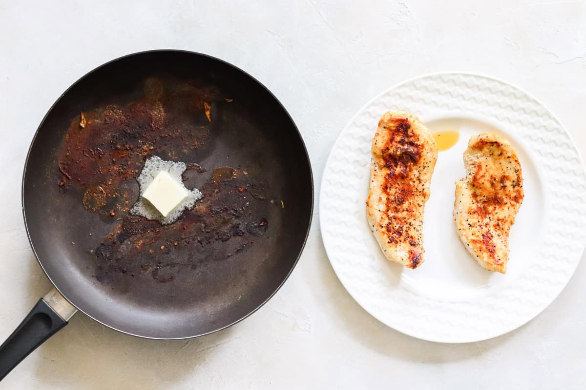 black skillet with butter melting next to a plate of cooked chicken that was just sauteed in the skillet.