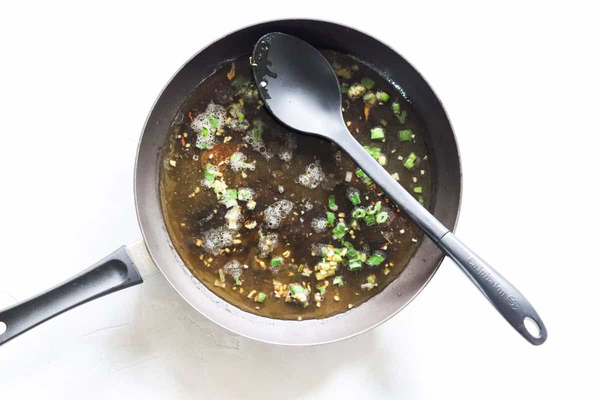 black skillet with green onions, garlic, butter, and broth cooking.