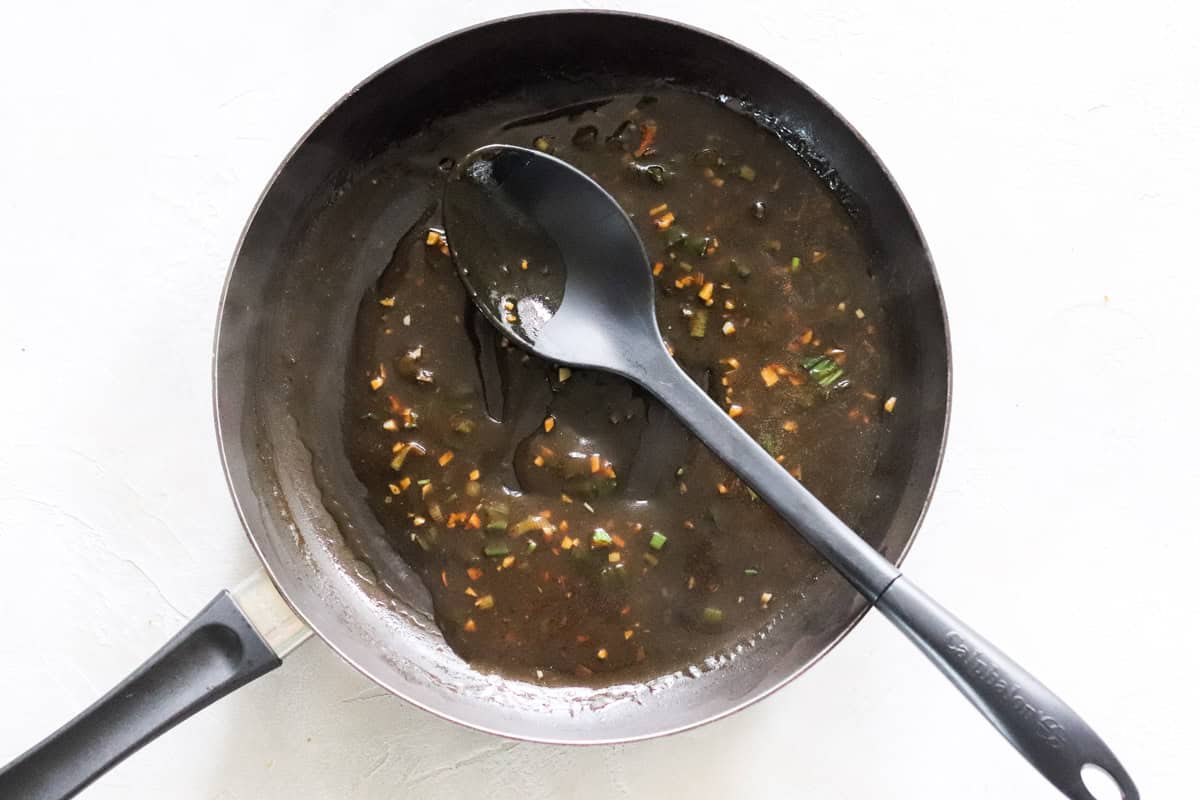 chicken gravy being stirred in a black skillet by a large black plastic spoon.