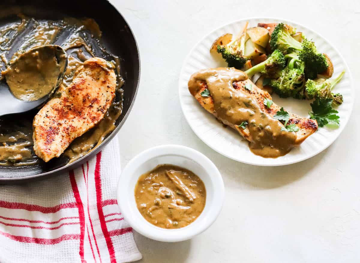 small bowl of homemade chicken gravy next to a skillet with chicken and gravy next to a plate of chicken, gravy, broccoli, and potatoes.