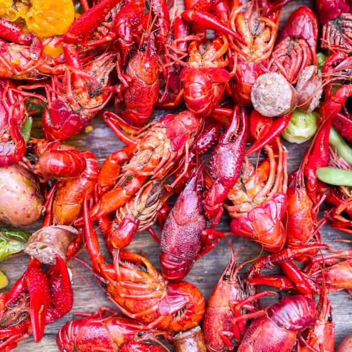 cooked crawfish with sausage, potatoes, jalapenos, and oranges on a wooden table at a crawfish boil.