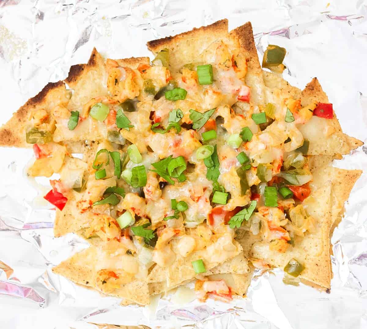 crawfish nachos on foil sprinkled with fresh parsley and green onions.