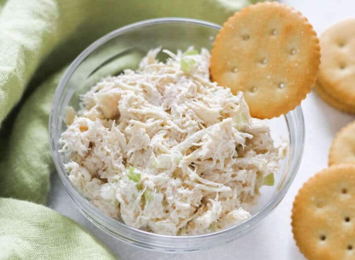 chicken salad and a ritz cracker in a glass bowl on white table with green napkin.