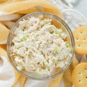 glass bowl with chicken salad on a yellow and white towel surrounded with butter crackers.