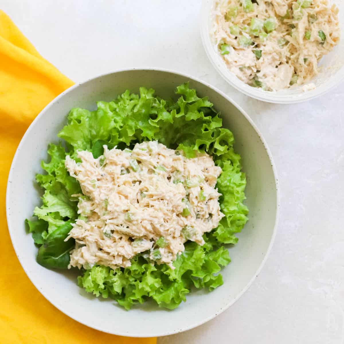 yellow napkin under a bowl of lettuce and chicken salad next to a bowl with extra chicken salad without mayo.