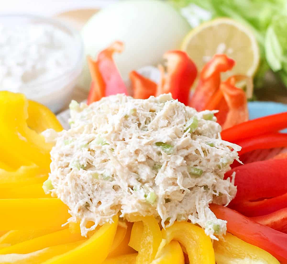 scoop of chicken salad on yellow and red bell peppers with onion, lemon, cottage cheese and celery in background.