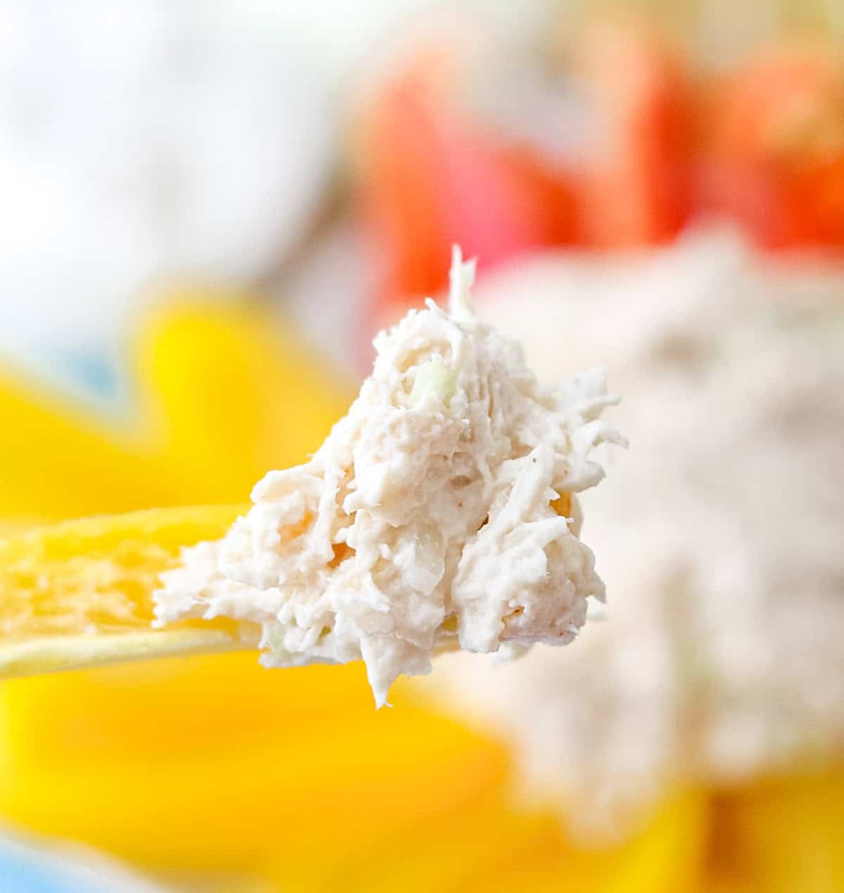 yellow bell pepper with a bite of chicken salad, with bell peppers and chicken salad blurred in background.