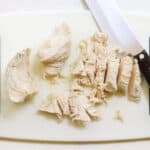 chicken breast chopped on a cutting board with a knife.