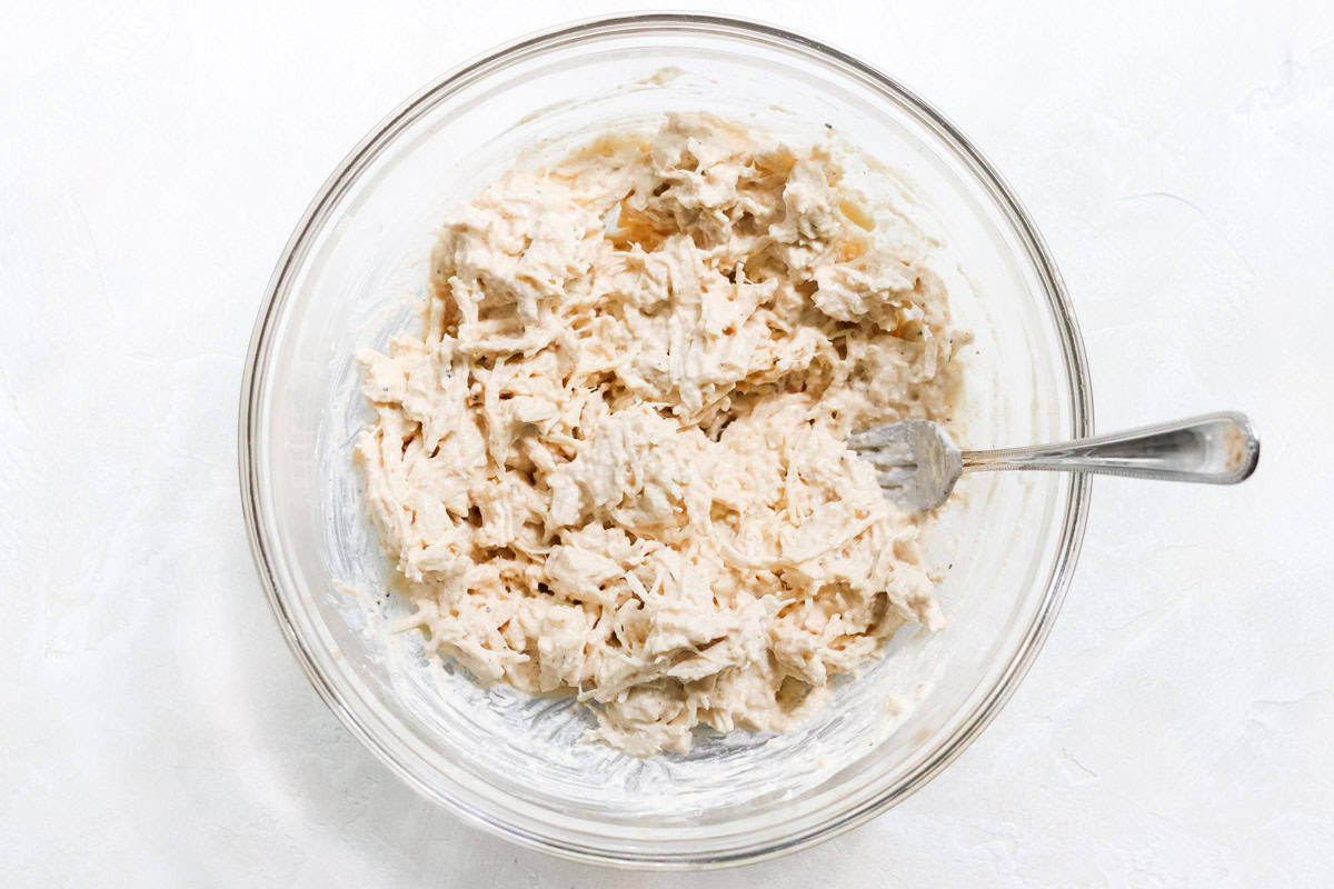 cottage cheese chicken salad stirred in a clear bowl with a silver fork.
