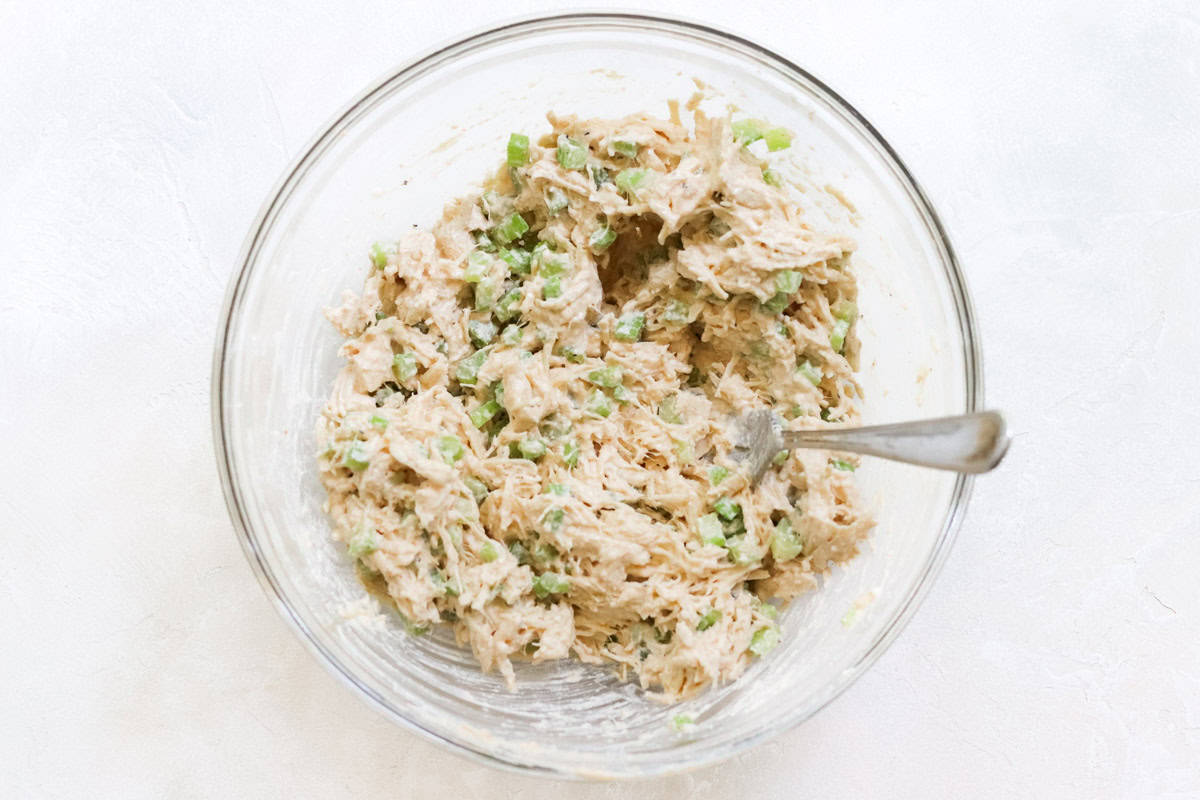 bowl of chicken salad stirred together with a silver fork.