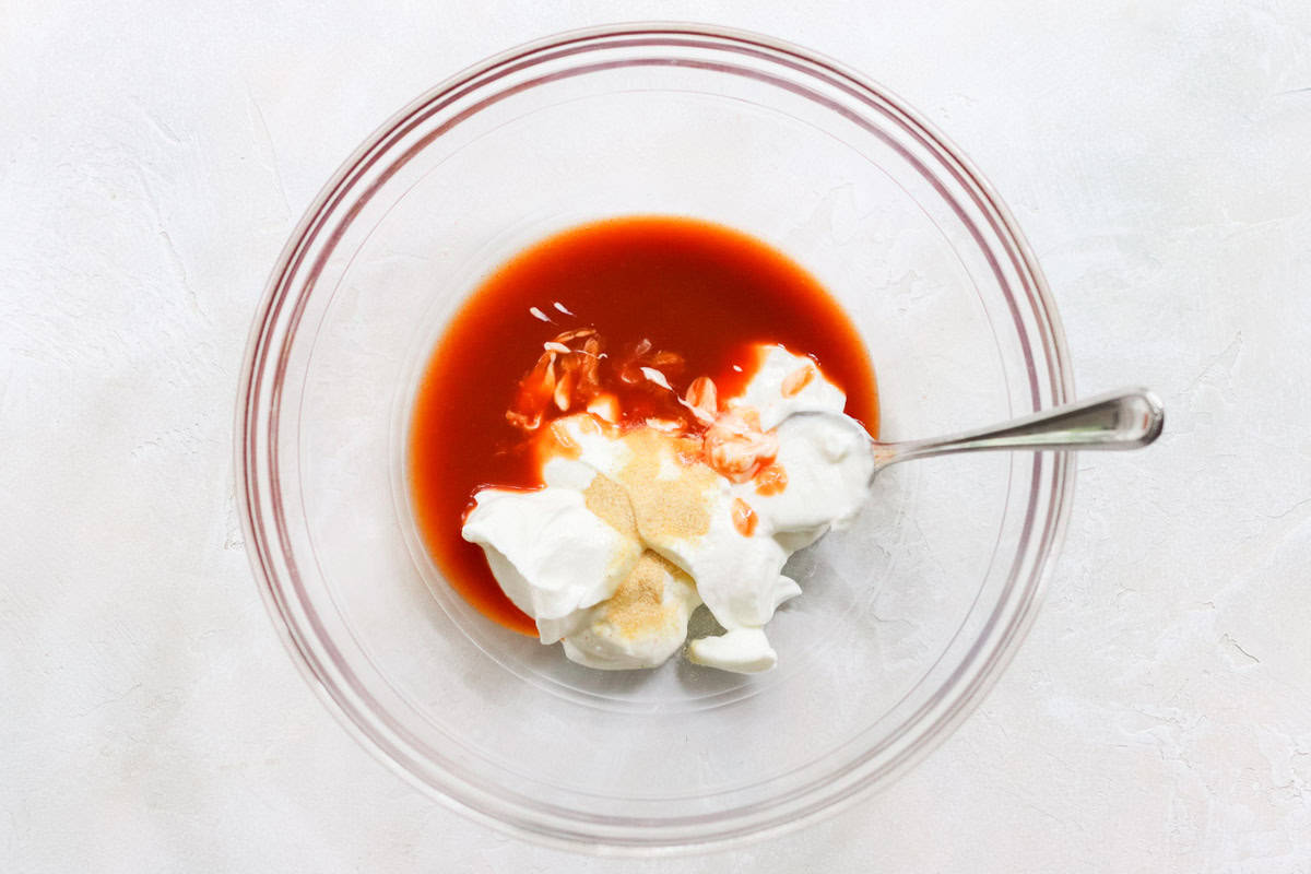 clear bowl with yogurt, buffalo wing sauce, and garlic powder with a silver spoon.