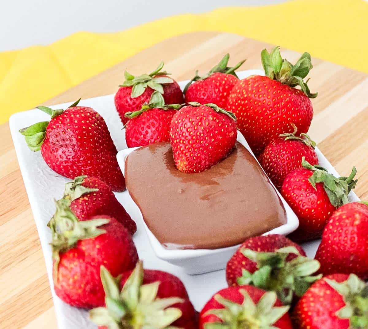plate of fresh strawberries with a bowl of chocolate sauce and a strawberry dipping into the sauce.