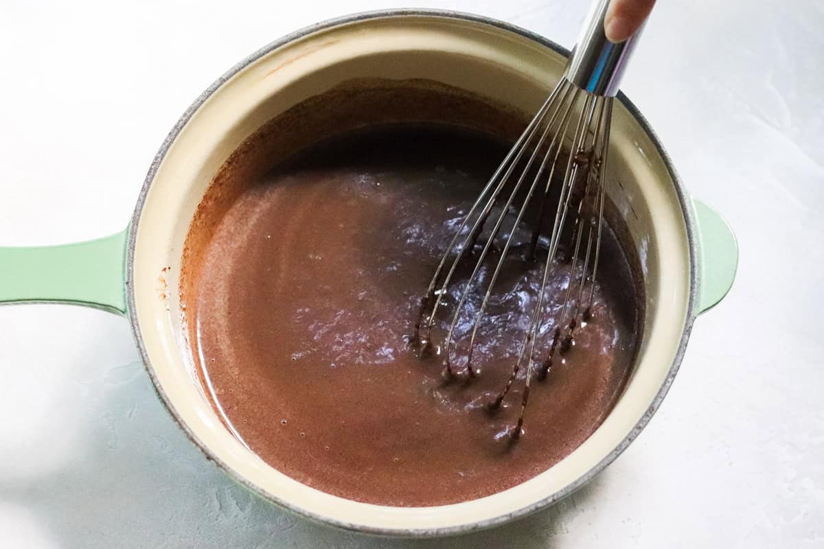 green saucepan with chocolate sauce being stirred together with a silver whisk.