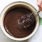hand whisking chocolate sauce together in a green saucepan.