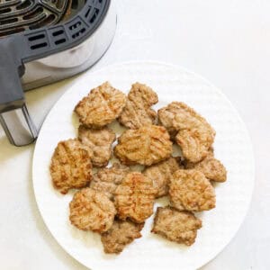 plate with cooked sausage next to the basket of an air fryer.