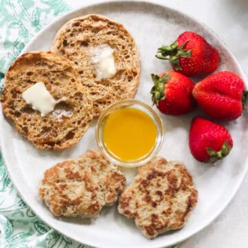 plate with two breakfast sausage patties, bowl of maple mustard sauce, fresh strawberries, and a buttered english muffin.