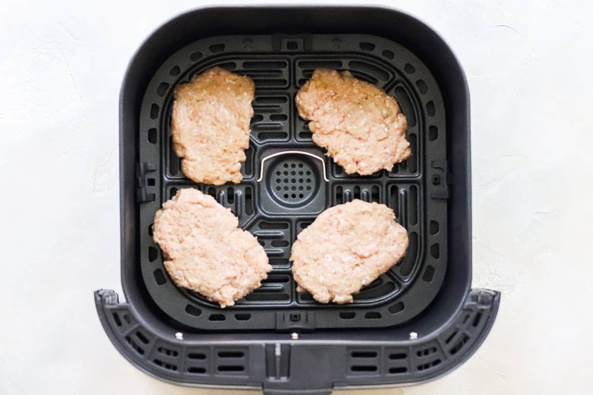 basket of air fryer filled with homemade breakfast sausage patties before cooking.