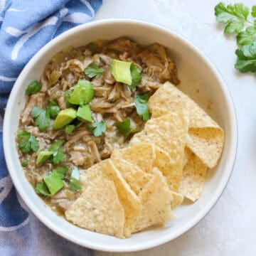 bowl of pork with avocado, cilantro, and tortilla chips next to fresh cilantro and a blue napkin.