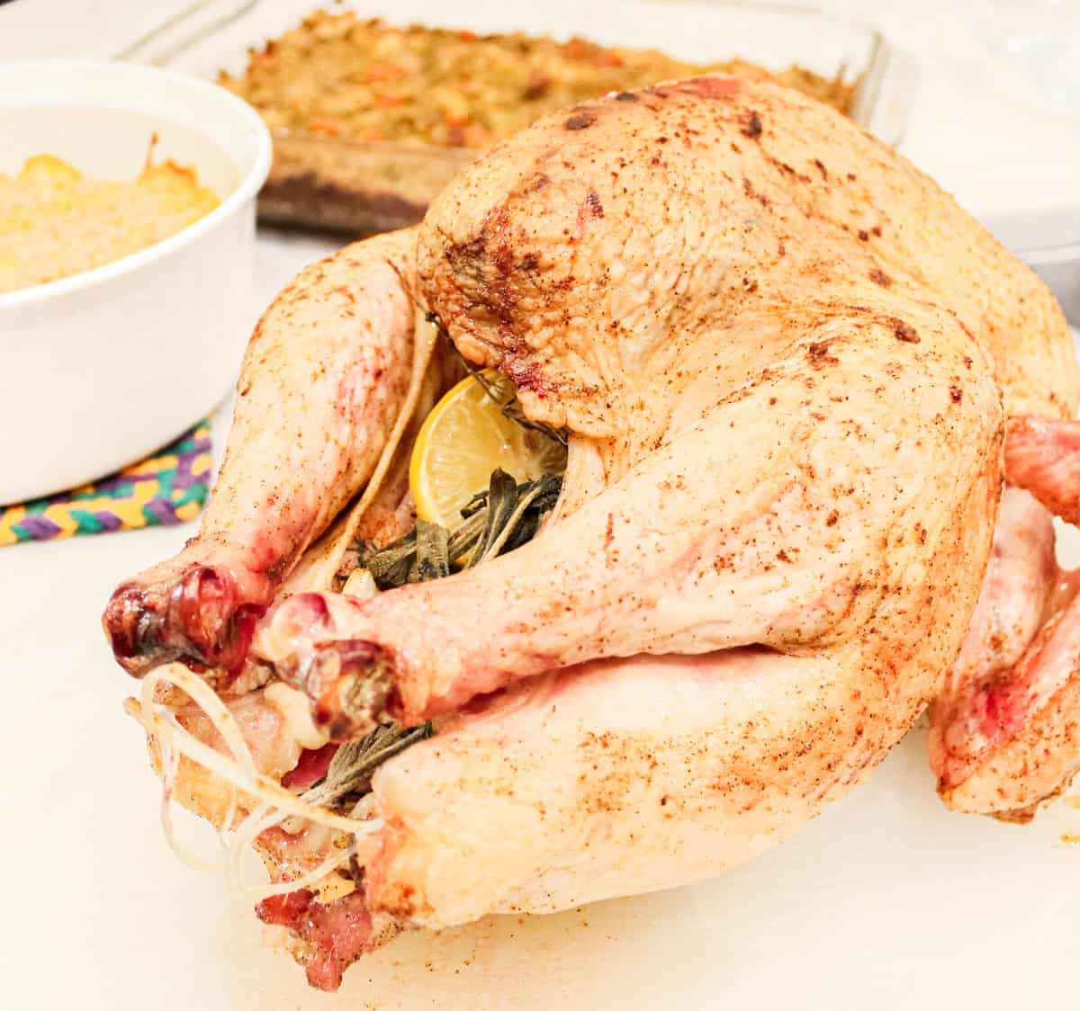 cooked thanksgiving turkey on a counter before cutting next to a casserole dish of squash casserole and stuffing.