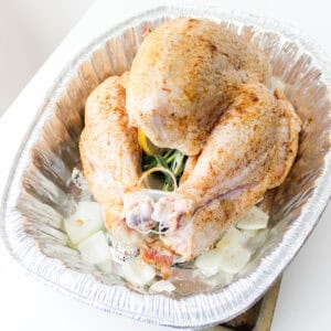 turkey in a DIY roasting rack that is seasoned, stuffed with herbs and lemon, and surrounded by chopped onions.
