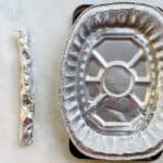 a piece of rolled foil next to a disposable roasting pan on a white counter.
