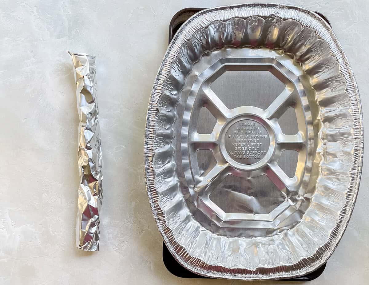 a piece of rolled foil next to a disposable roasting pan on a white counter.