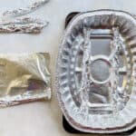 sheet of rolled foil next to a disposable roasting pan on a baking sheet.