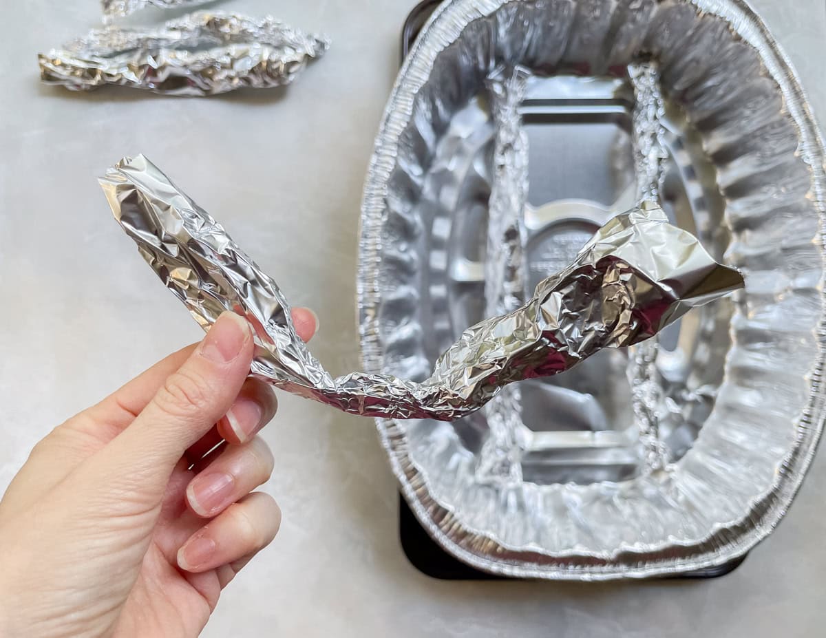hand holding a piece of rolled foil over a DIY roasting rack.