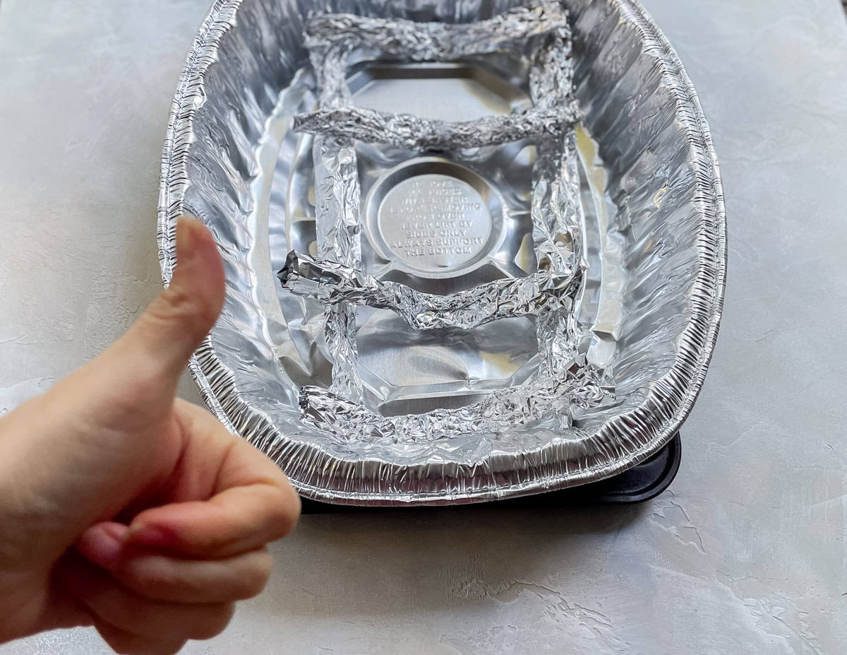DIY roasting rack made from aluminum foil on a baking sheet with a white hand giving a thumbs up.
