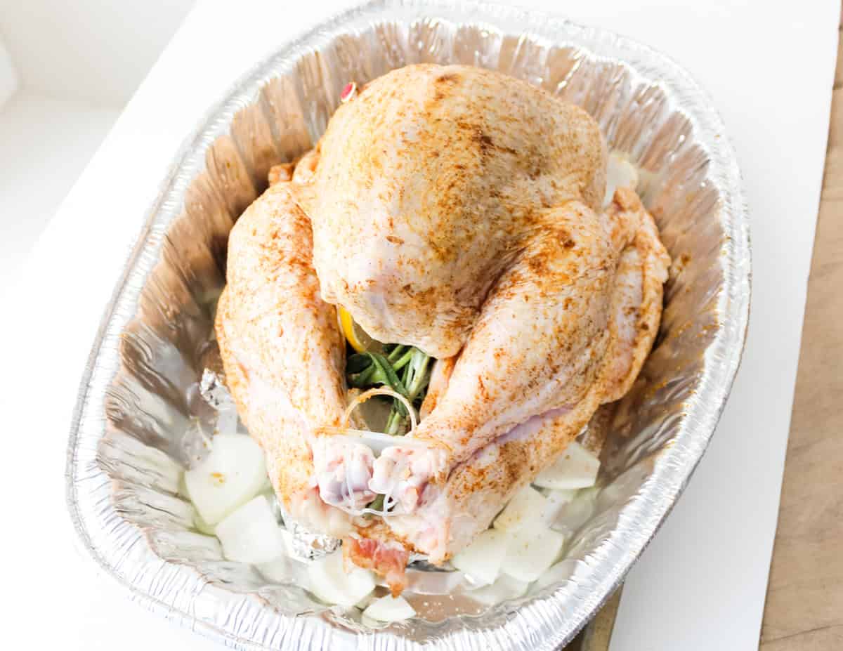 thanksgiving turkey in a DIY roasting rack that is seasoned, stuffed with herbs and lemon, and surrounded by chopped onions.