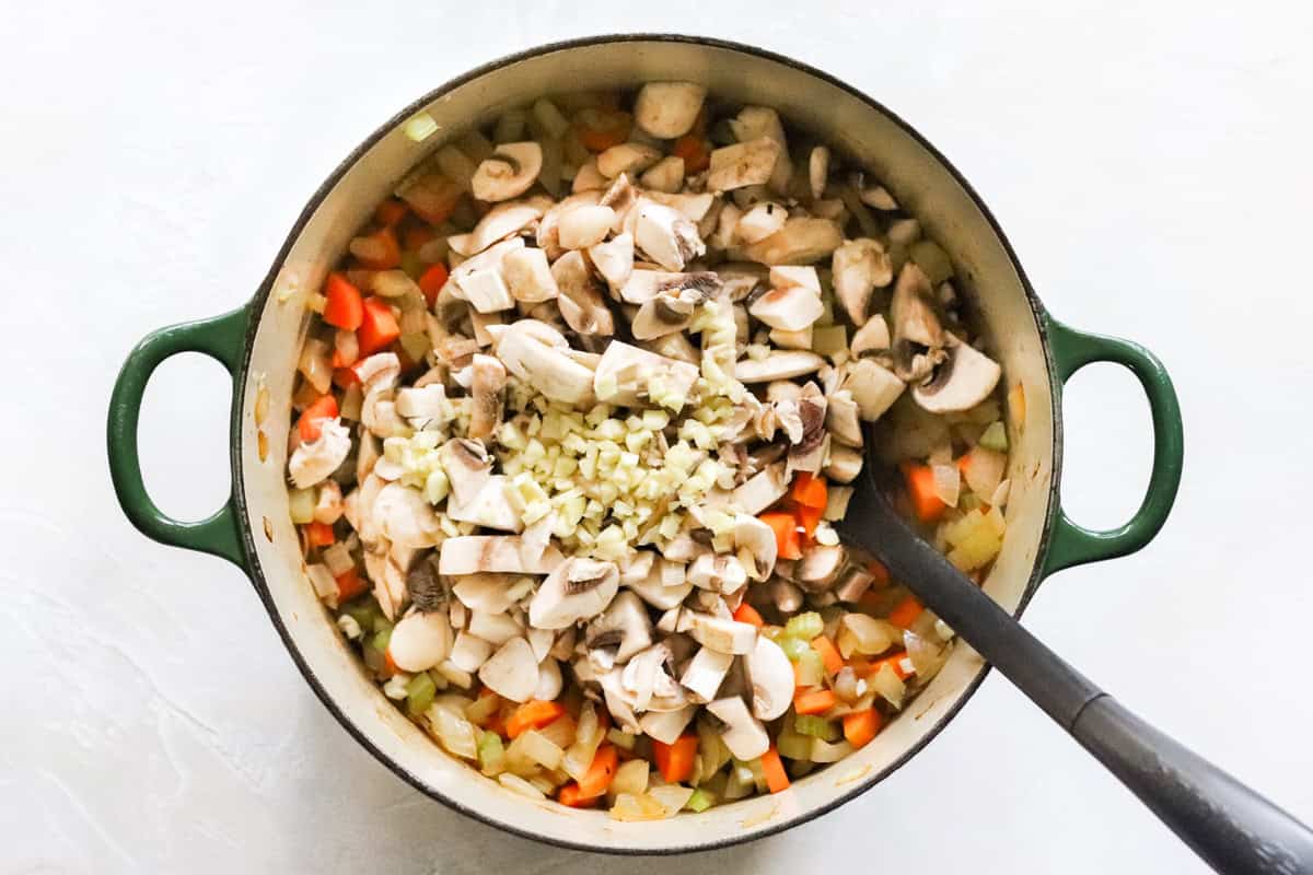 mushroom and garlic added to a pot of sauteed onions, carrots, and celery.