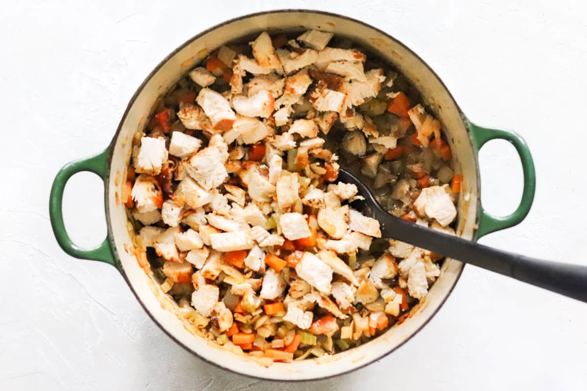 chicken added to a pot with cooked veggies.