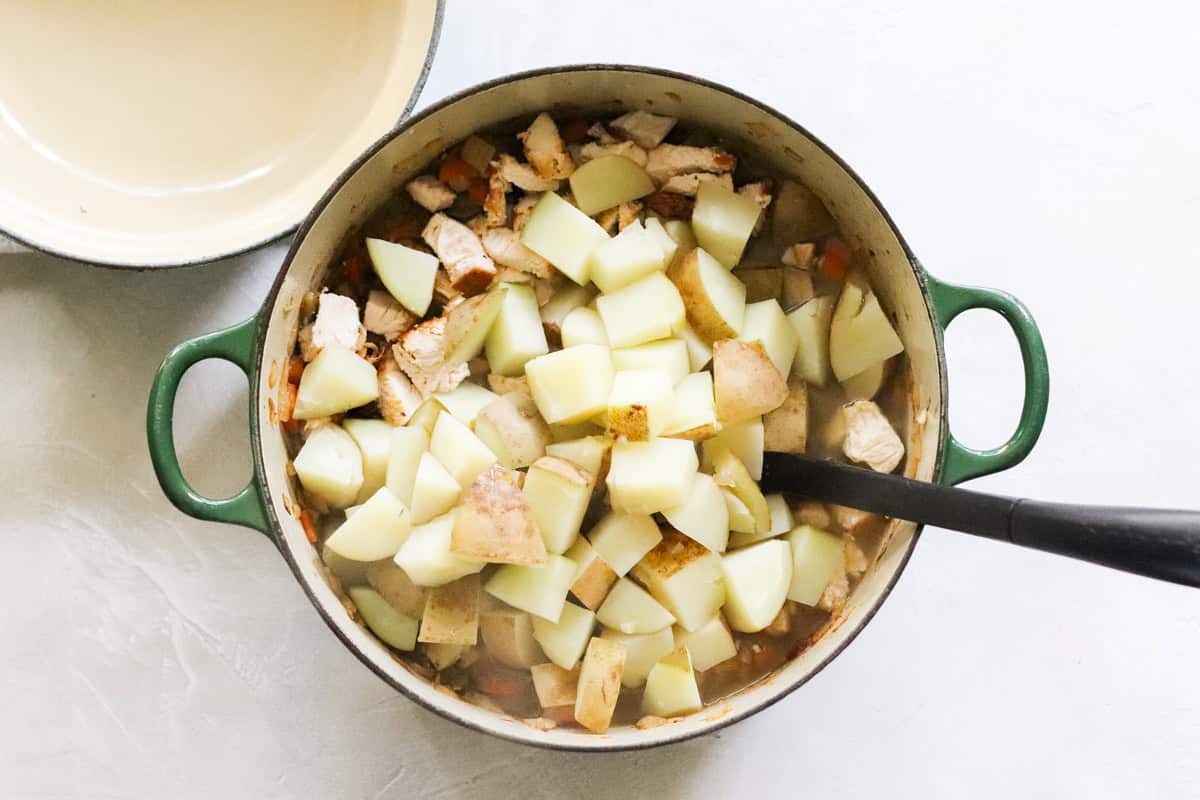 green pot of stew with cooked potatoes added next to an empty pot.