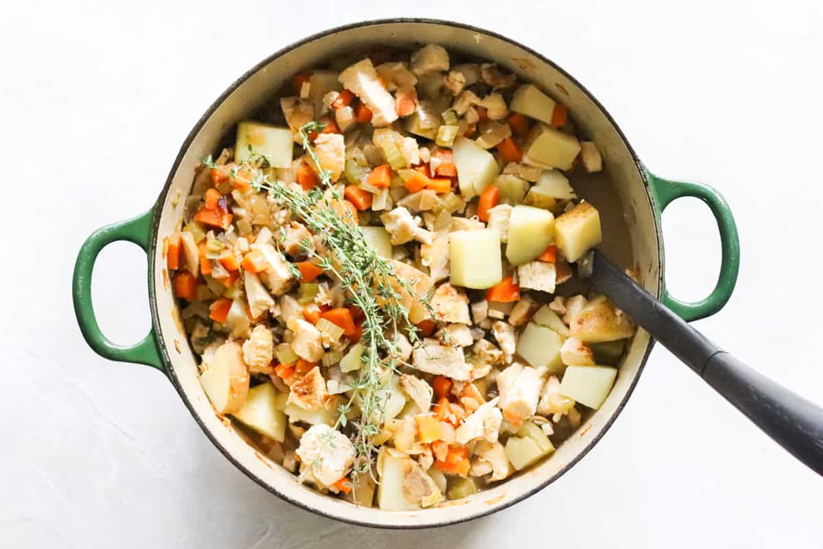 pot of chicken hash while cooking with fresh thyme and a black spoon stirring it.
