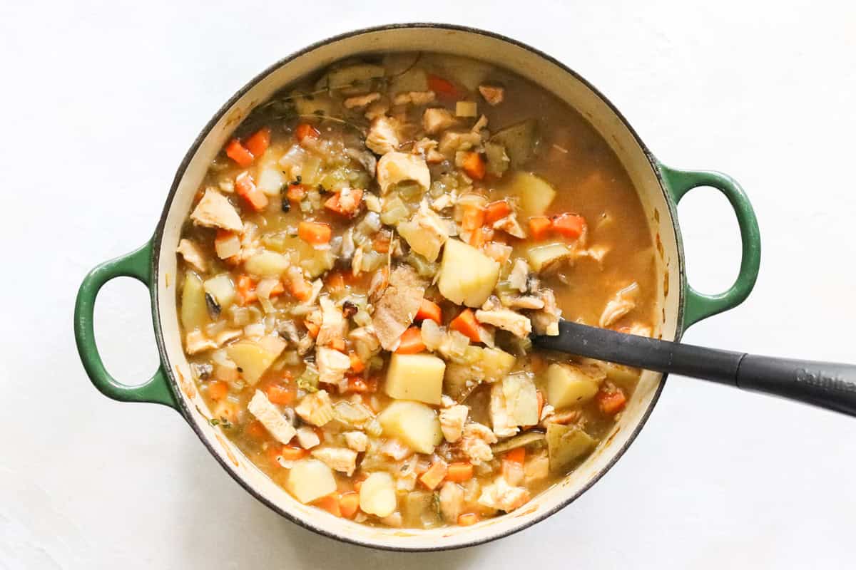 green dutch oven with simmering chicken hash being stirred by a black spoon.
