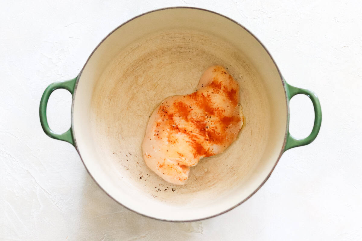 seasoned chicken breast cooking in a green dutch oven.