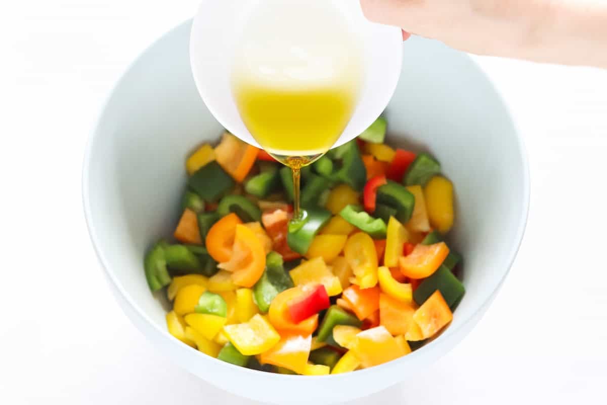 olive oil being drizzled over a bowl of chopped bell peppers.