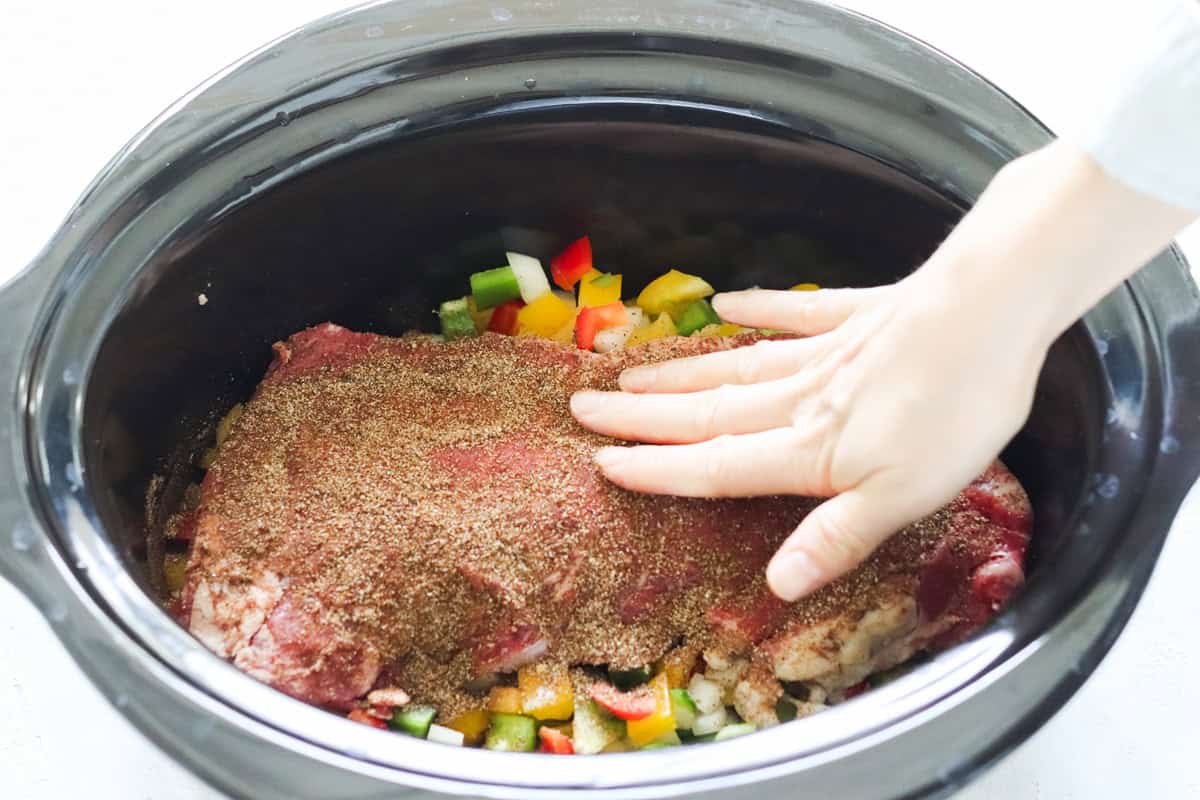hand pressing spices into flank steak in a slow cooker.