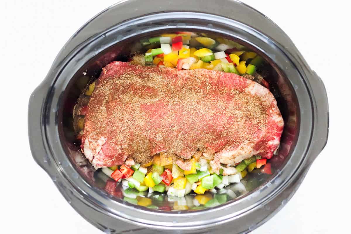 spice rubbed beef roast over bell peppers and onions in a slow cooker before cooking.