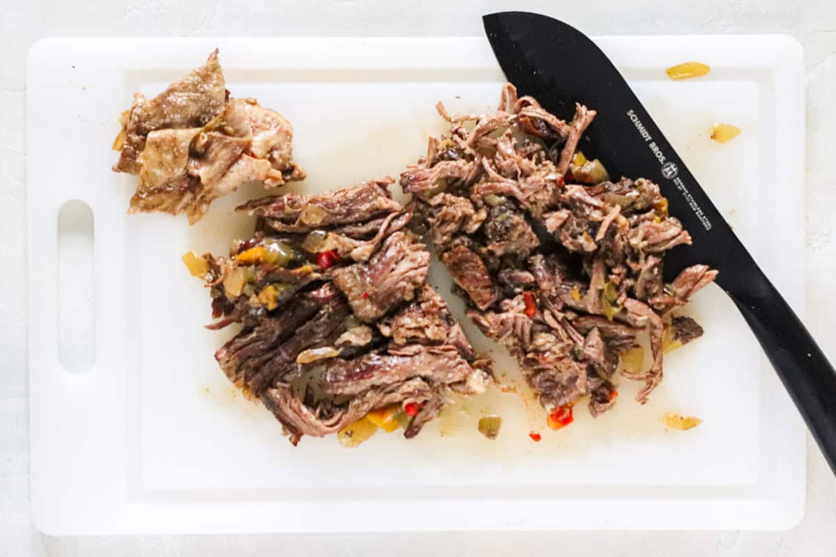 shredded meat chopped on a cutting board for beef carnitas tacos.