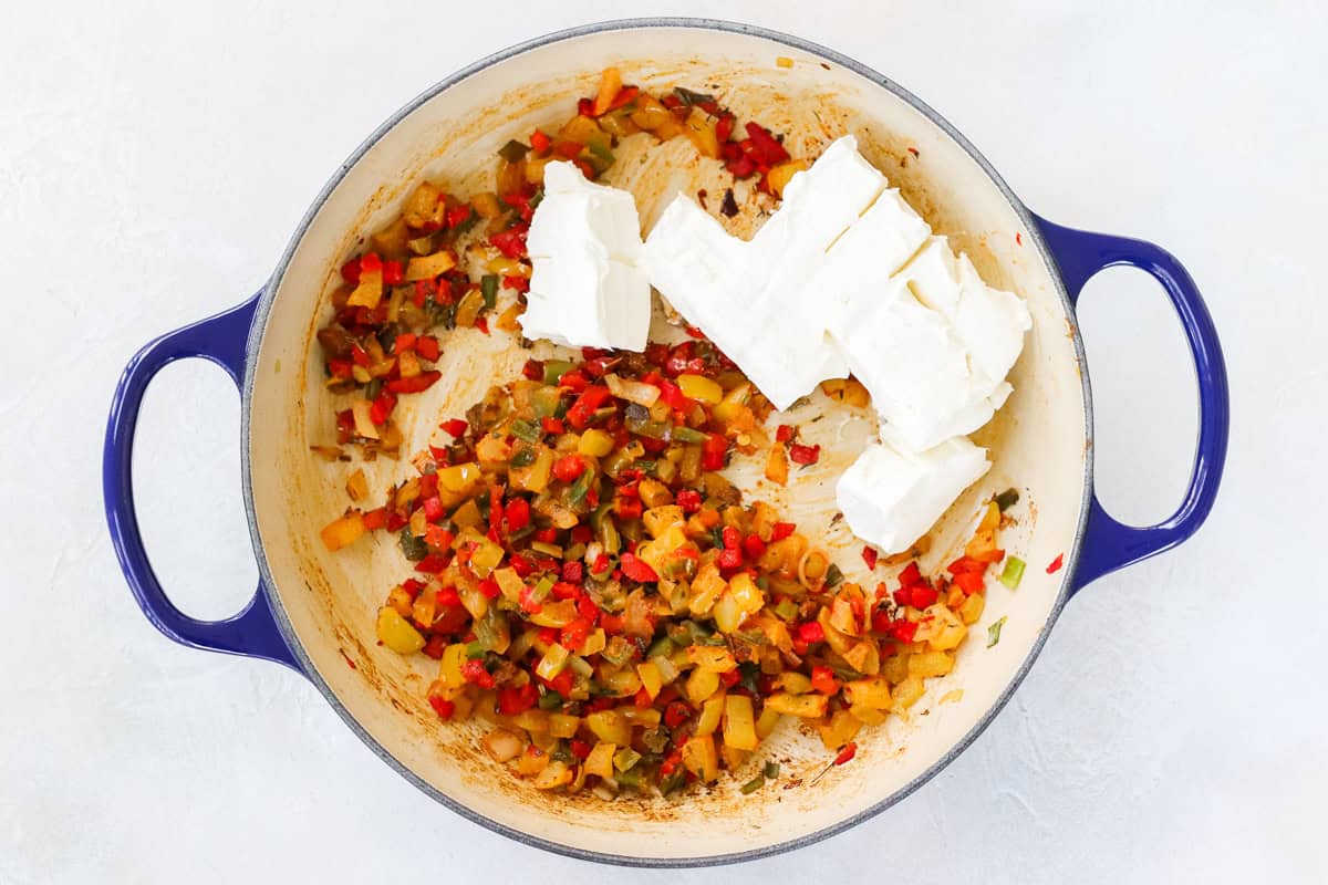 sauteed veggies with spices in a blue pan with chopped cream cheese before stirring.