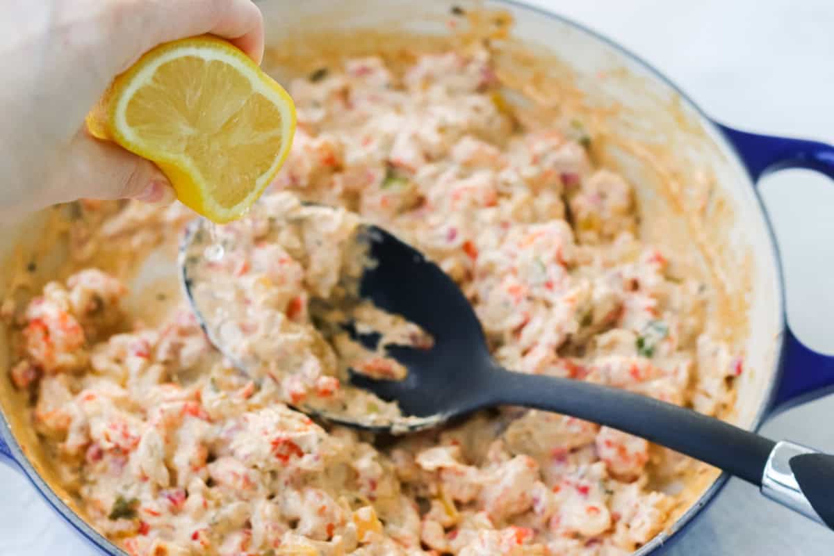 hand squeezing lemon into crawfish dip in a blue pan with a black slotted spoon.