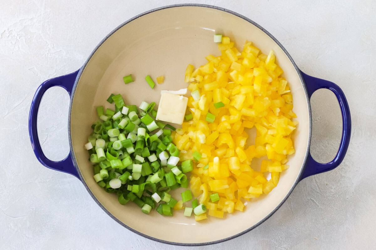 blue pan with butter, chopped green onions, and diced yellow bell pepper before cooking.